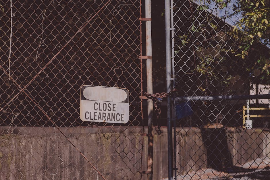 Close-up photograph of a glass door with a silver metallic frame and a keyhole, featuring a white rectangular hanging sign displaying the word 'GESCHLOSSEN' in bold black letters, indicating the estab