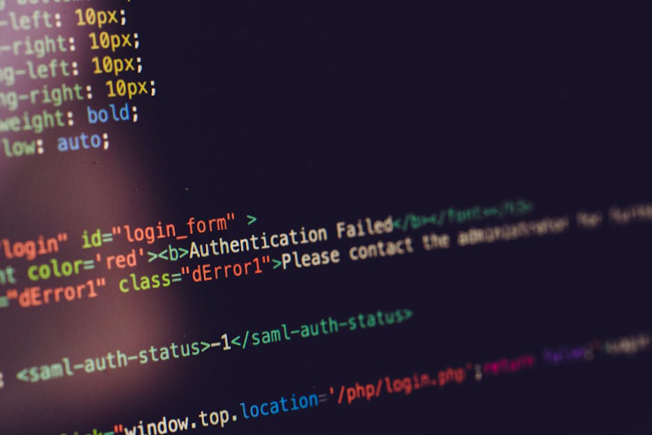 A close-up view of a person's right hand with a wristwatch, typing on a silver laptop keyboard placed on a wooden surface. The laptop screen displays lines of code in a text editor, with a dark backgr